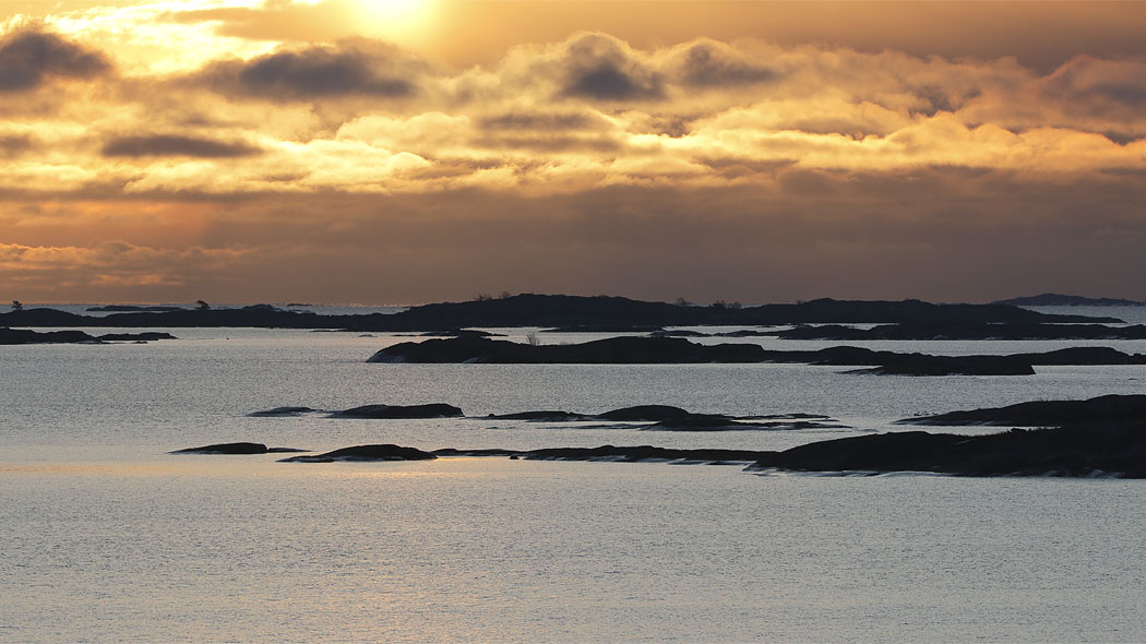 Skärgårdens holmar och öar som silhuetter i motljus på en lugn dag.